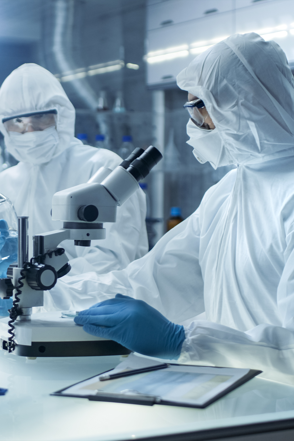 Two people in full PPE looking through a microscope