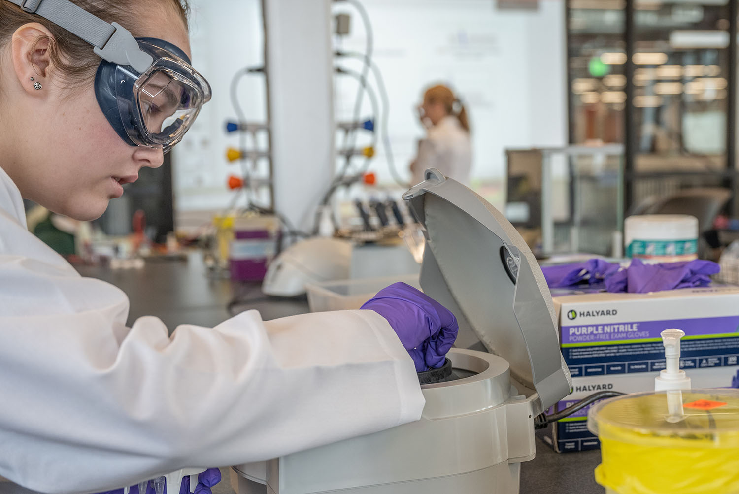 Woman wearing lab coat and goggles working in a lab.